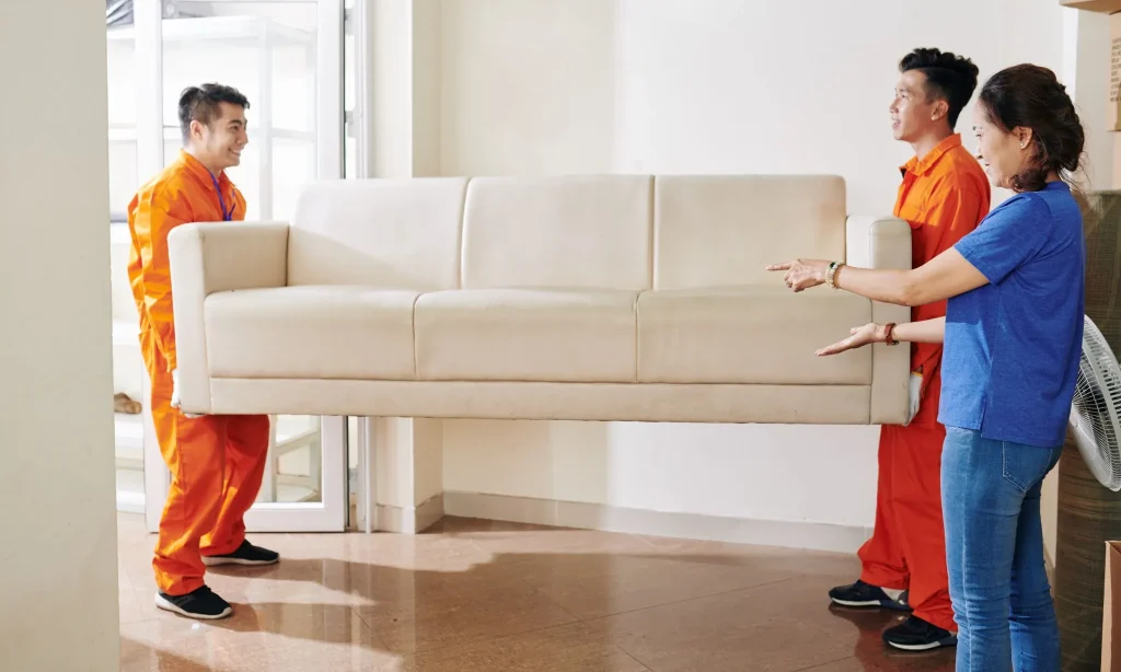 Beberapa pekerja dari perusahaan jasa pindahan sedang mengangkat perabotan dengan hati-hati.