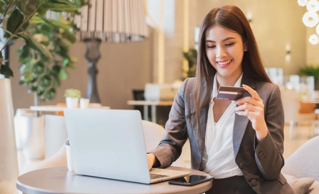 Tangan seseorang memegang kartu debit di depan sebuah laptop.