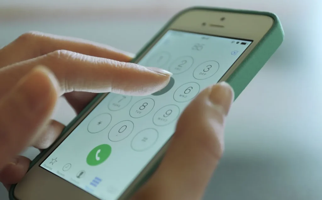 Tangan seseorang sedang menekan nomor darurat di smartphone.