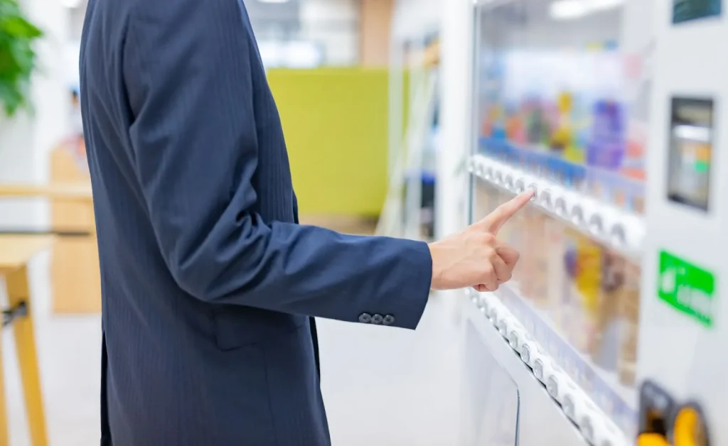 Tangan seseorang sedang memasukkan koin ke dalam mesin penjual otomatis.