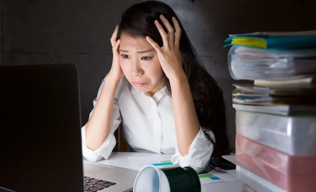 Seorang pekerja terlihat sangat stres dan kelelahan di meja kerjanya.