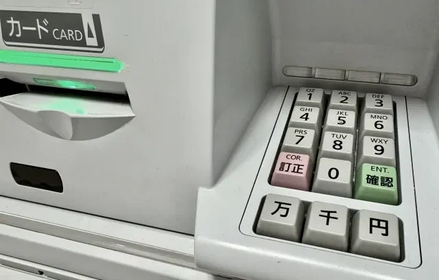 Tangan seseorang sedang menekan tombol di mesin ATM.