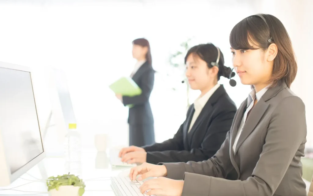 Tampilan meja kerja seorang staf customer service dengan komputer dan telepon.